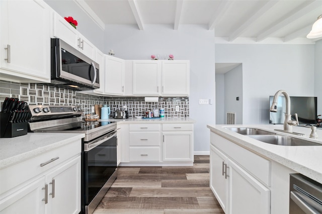 kitchen featuring stainless steel appliances, tasteful backsplash, white cabinets, a sink, and beamed ceiling