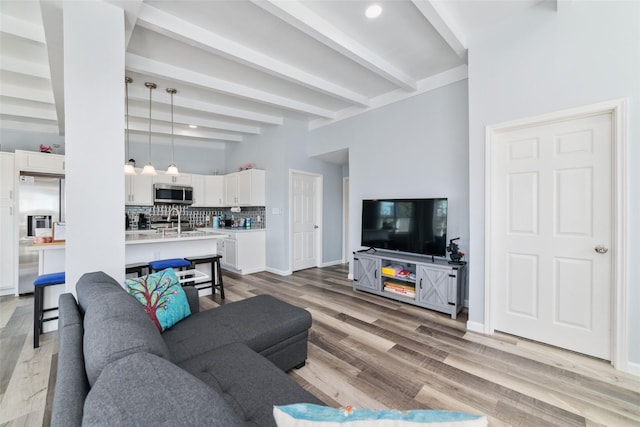 living area with light wood-type flooring, baseboards, and beamed ceiling