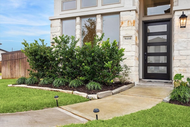 entrance to property with stone siding, a yard, and fence