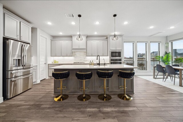 9410 Knollwood Ln, Missouri City, TX 77459 - kitchen with visible vents, an island with sink, appliances with stainless steel finishes, decorative light fixtures, and light countertops