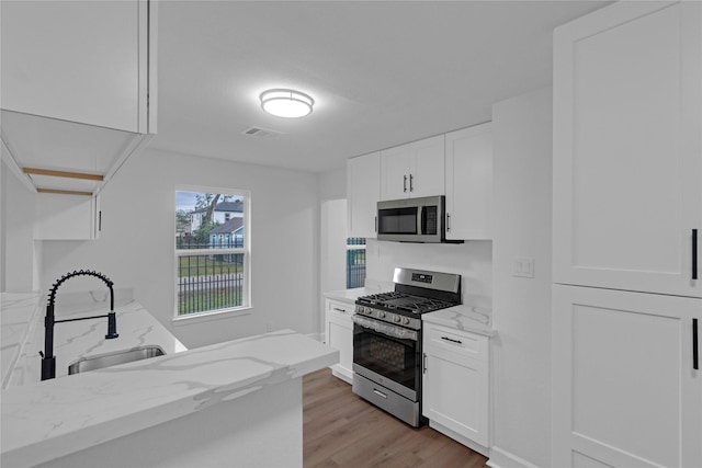 kitchen with visible vents, white cabinets, light stone counters, stainless steel appliances, and a sink