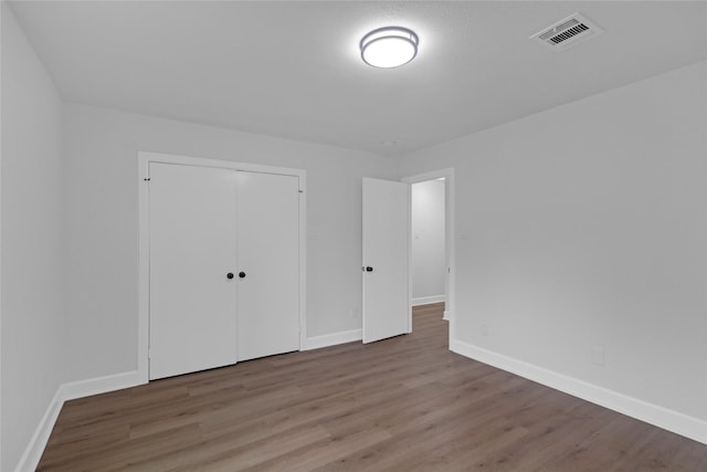 unfurnished bedroom with baseboards, a closet, visible vents, and wood finished floors