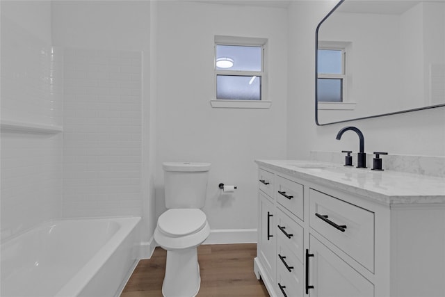 bathroom featuring baseboards, bathing tub / shower combination, toilet, wood finished floors, and vanity