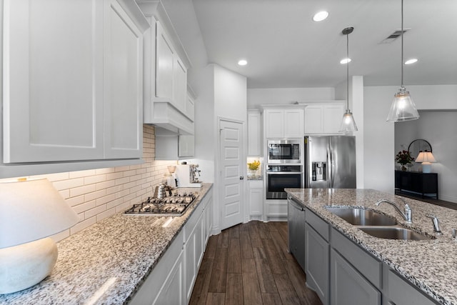 kitchen with hanging light fixtures, appliances with stainless steel finishes, white cabinetry, a sink, and light stone countertops