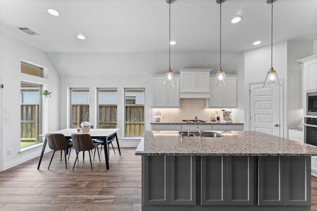 kitchen featuring a center island with sink, visible vents, decorative light fixtures, light stone countertops, and white cabinetry