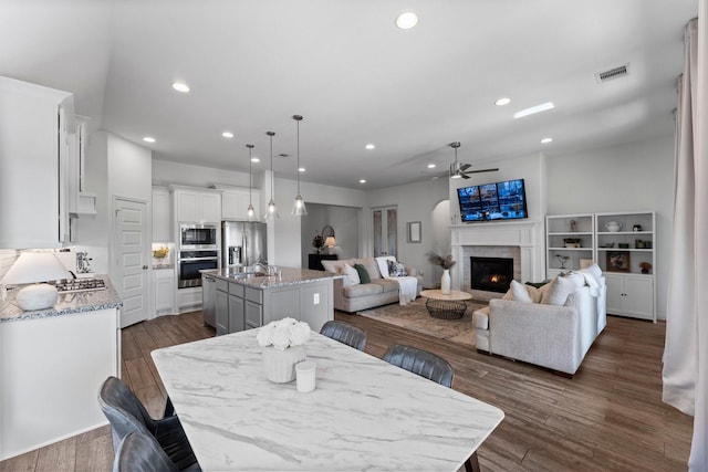 dining area featuring a warm lit fireplace, visible vents, ceiling fan, dark wood-style flooring, and recessed lighting