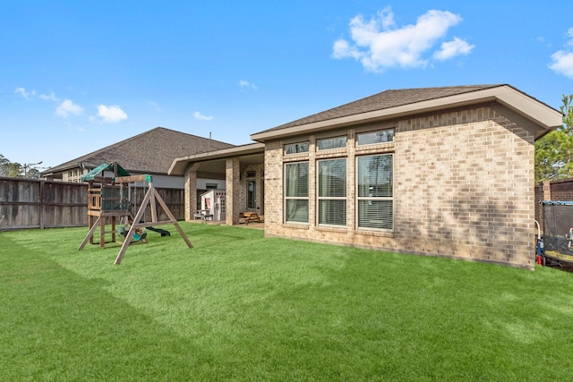 back of property with a yard, a playground, fence, and brick siding