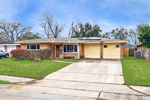 single story home with central AC unit, an attached garage, brick siding, driveway, and roof mounted solar panels