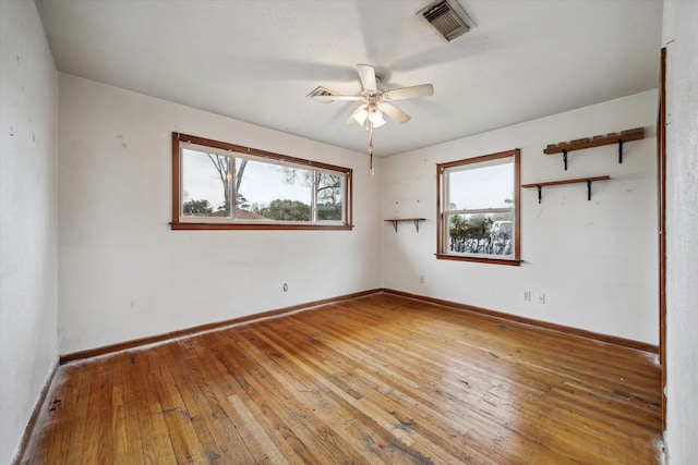 empty room featuring a ceiling fan, wood finished floors, visible vents, and baseboards