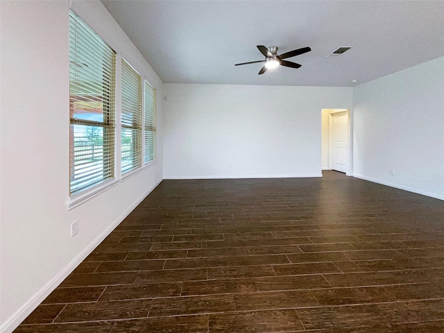 unfurnished room with a ceiling fan, visible vents, dark wood finished floors, and baseboards