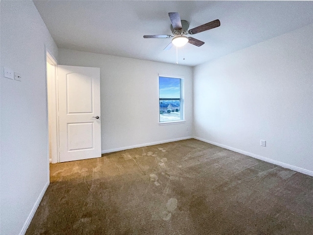 spare room featuring a ceiling fan, dark carpet, and baseboards