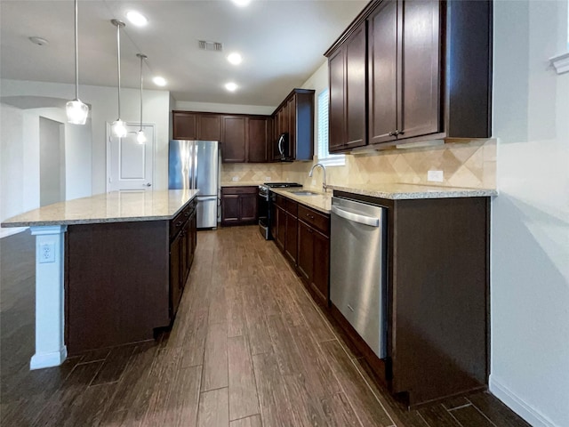 kitchen featuring light stone counters, a center island, pendant lighting, appliances with stainless steel finishes, and dark wood-type flooring