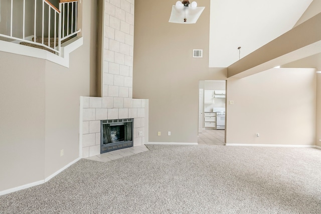 unfurnished living room with light colored carpet, a fireplace, a towering ceiling, baseboards, and visible vents