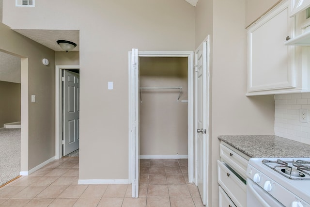 kitchen featuring light tile patterned floors, decorative backsplash, white cabinetry, light stone countertops, and baseboards