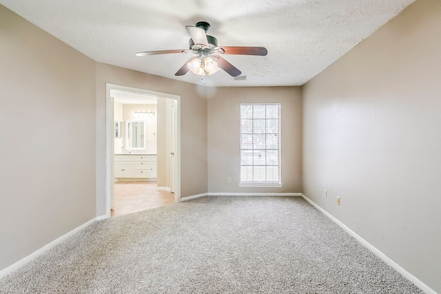 empty room with light carpet, a textured ceiling, a ceiling fan, and baseboards