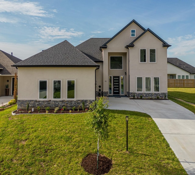 view of front facade with stone siding, a front lawn, roof with shingles, and stucco siding