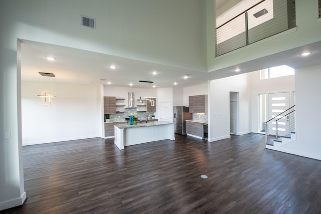 unfurnished living room with dark wood-style flooring, a towering ceiling, visible vents, stairs, and baseboards