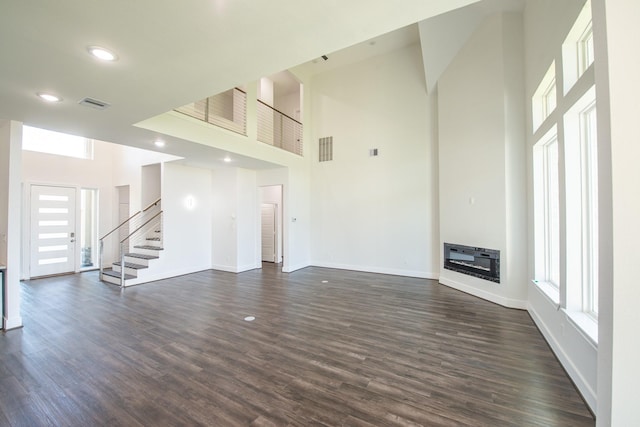 unfurnished living room featuring dark wood-style floors, a high ceiling, visible vents, and a glass covered fireplace