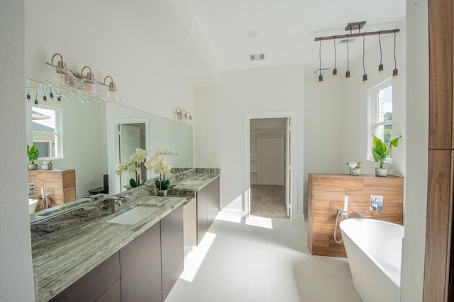 bathroom with a walk in closet, a freestanding tub, visible vents, and vanity