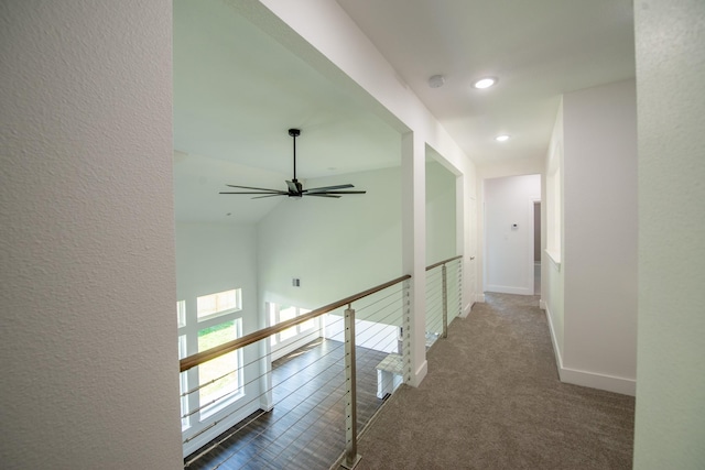 corridor with dark colored carpet, a textured wall, baseboards, and recessed lighting