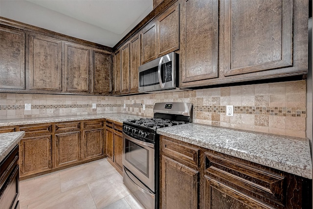 kitchen with appliances with stainless steel finishes, light tile patterned floors, light stone counters, and tasteful backsplash