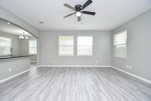 unfurnished living room with light wood-style floors, arched walkways, visible vents, and baseboards