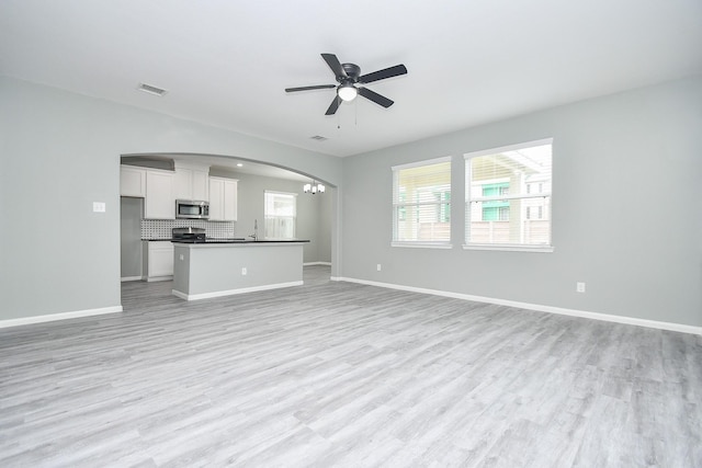 unfurnished living room featuring light wood-type flooring, baseboards, visible vents, and ceiling fan with notable chandelier