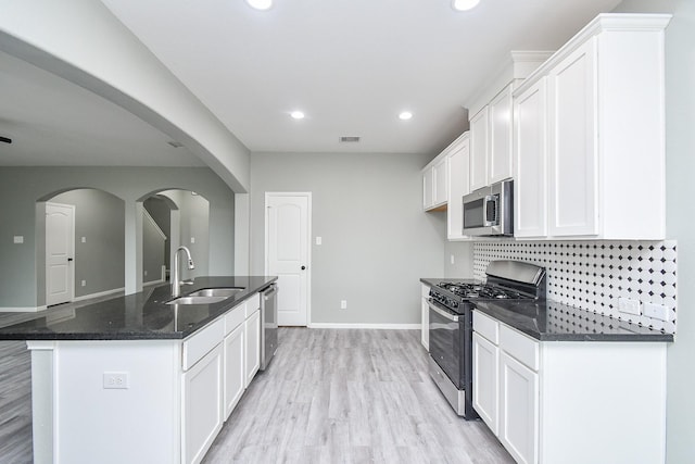 kitchen with stainless steel appliances, white cabinets, a sink, and a center island with sink