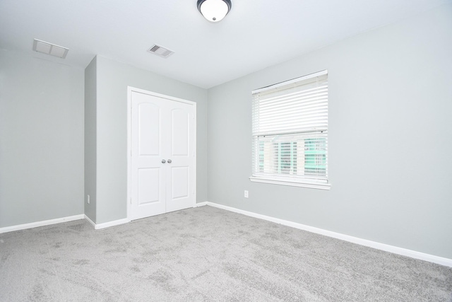 unfurnished bedroom with baseboards, visible vents, a closet, and light colored carpet