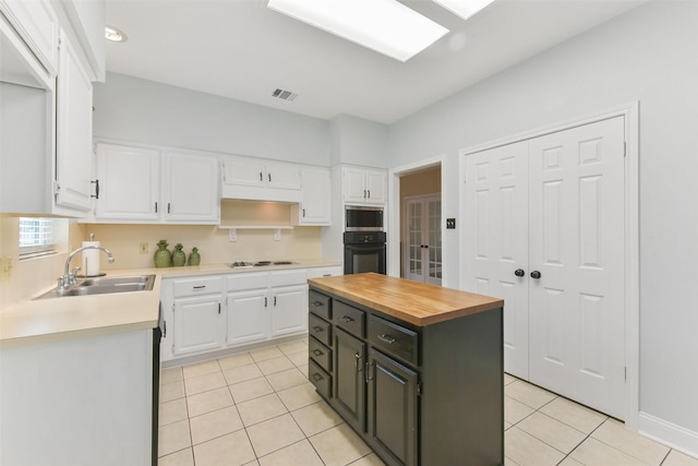 kitchen with oven, visible vents, white cabinetry, white cooktop, and a center island