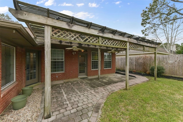 rear view of property with ceiling fan, a patio, brick siding, fence, and a lawn