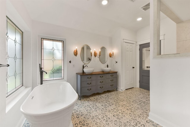 bathroom with a sink, visible vents, baseboards, a soaking tub, and double vanity