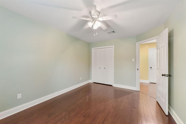 unfurnished bedroom featuring ceiling fan, wood finished floors, visible vents, baseboards, and a closet