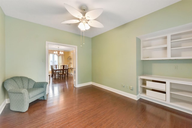 living area with dark wood-style flooring, baseboards, and ceiling fan with notable chandelier