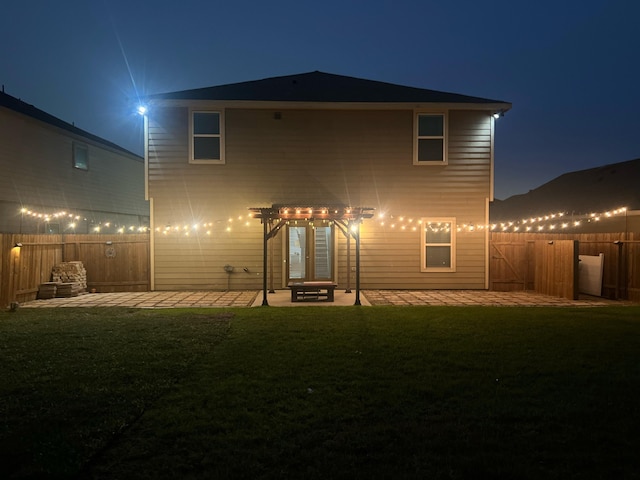 back of house at night with a patio area, a lawn, and fence