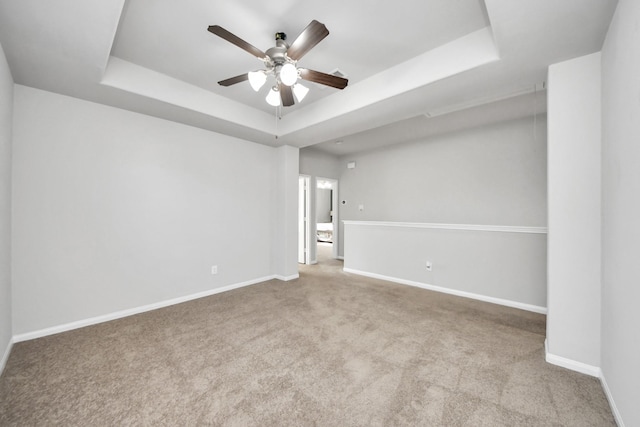 spare room featuring carpet floors, a tray ceiling, baseboards, and a ceiling fan