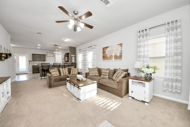 living area featuring light carpet, ceiling fan with notable chandelier, visible vents, and baseboards