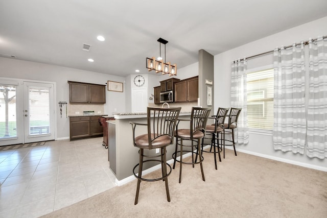 kitchen with light tile patterned floors, a breakfast bar area, a peninsula, dark brown cabinets, and stainless steel microwave