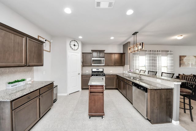 kitchen featuring visible vents, a breakfast bar, a peninsula, stainless steel appliances, and a sink