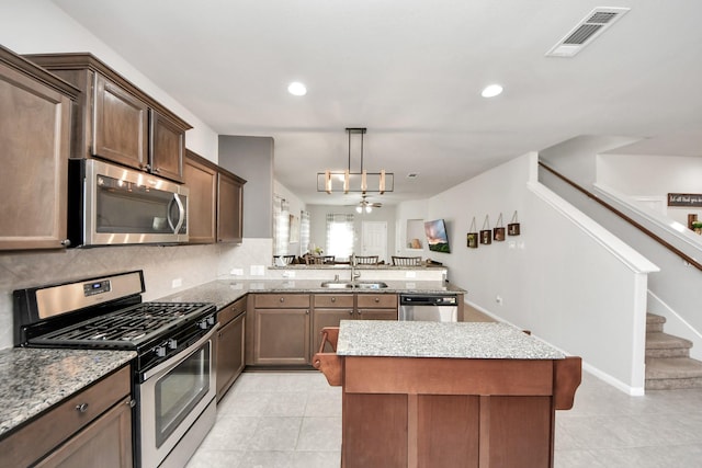 kitchen featuring stainless steel appliances, light stone counters, a sink, and visible vents