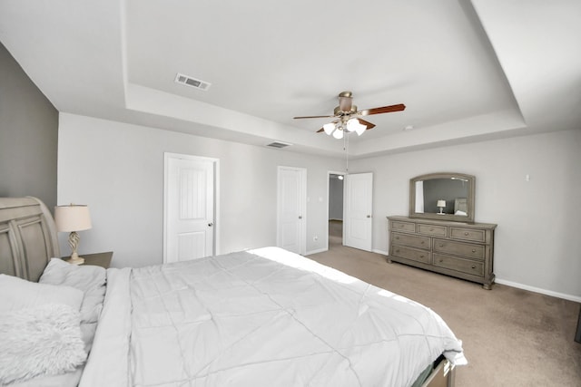 bedroom with a tray ceiling, light carpet, visible vents, and baseboards