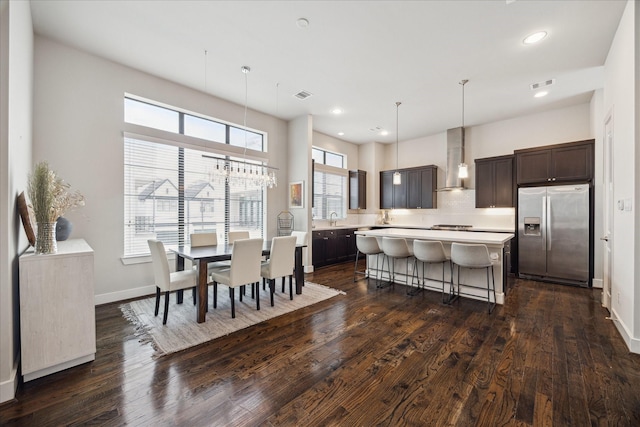 kitchen featuring stainless steel fridge, a center island, light countertops, wall chimney range hood, and pendant lighting