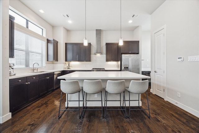 kitchen with stainless steel appliances, wall chimney range hood, light countertops, and a center island