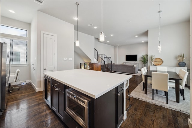 kitchen featuring a center island, wine cooler, light countertops, hanging light fixtures, and appliances with stainless steel finishes