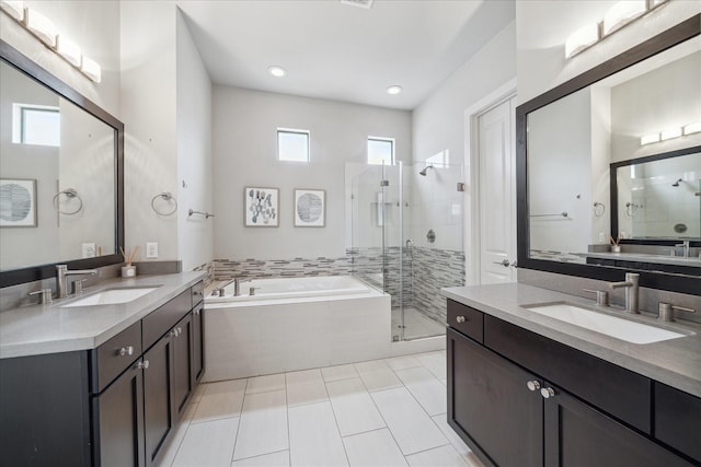 bathroom with two vanities, a stall shower, a garden tub, and a sink