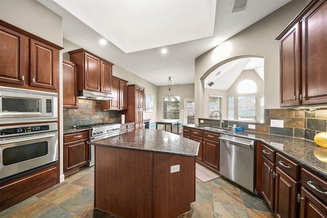 kitchen with a kitchen island, hanging light fixtures, stainless steel appliances, under cabinet range hood, and a sink