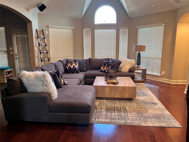 living room featuring lofted ceiling, baseboards, arched walkways, and dark wood-style flooring