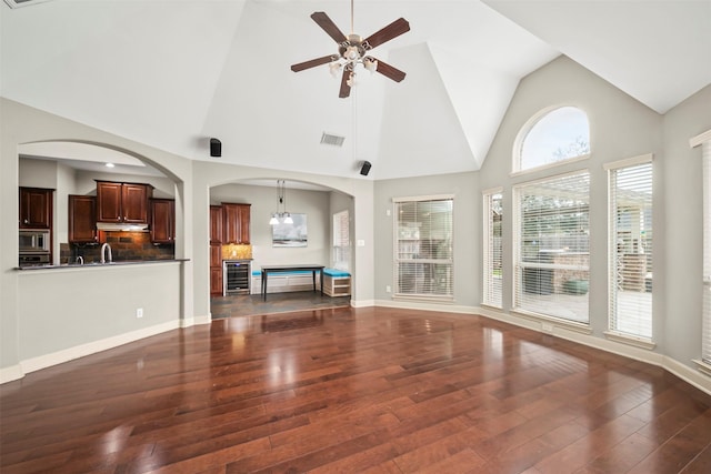 unfurnished living room featuring baseboards, visible vents, dark wood finished floors, ceiling fan, and high vaulted ceiling