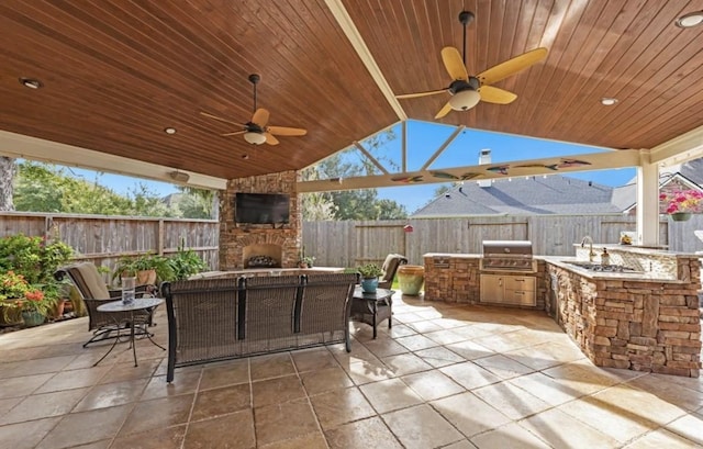 view of patio / terrace featuring an outdoor kitchen, a fenced backyard, an outdoor stone fireplace, a sink, and a grill