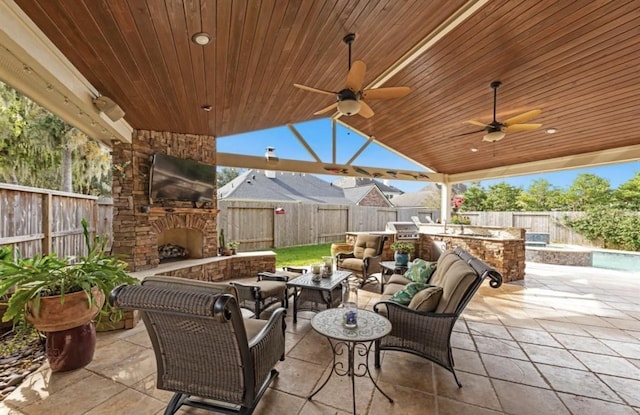 view of patio / terrace with exterior kitchen, an outdoor stone fireplace, a fenced backyard, and a ceiling fan